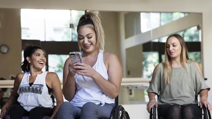 kvinne i rullestol sammen med venner, ser på mobiltelefon