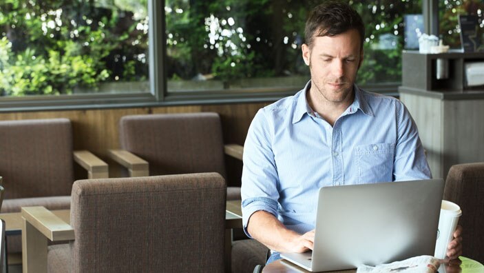 mann sitter foran datamaskin på kafe